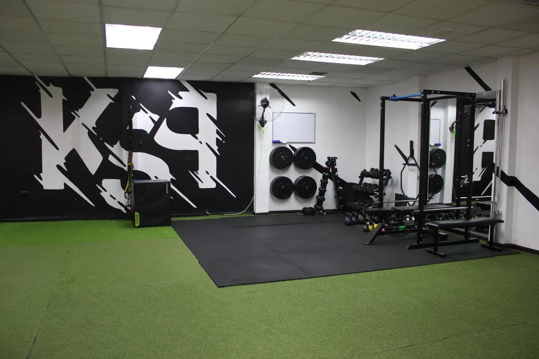 Sala de entrenamiento con el mural KSP, rack de sentadillas, discos y mancuernas sobre piso de caucho